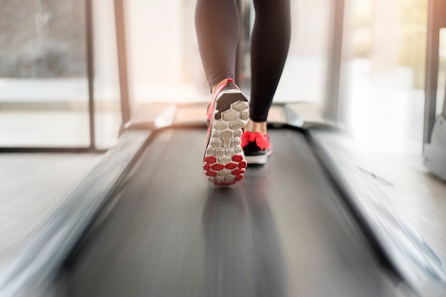 Foto chiuda su dei piedi muscolosi delle gambe della donna che corrono sull'allenamento di pedana mobile alla palestra di forma fisica