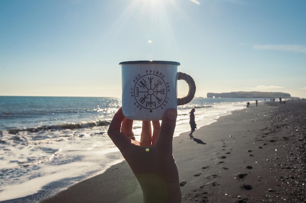 Close up woman showing enamel cup on beach concept photo