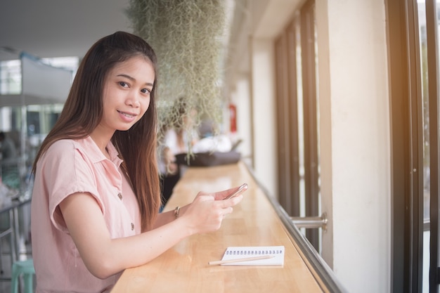 Close up. Woman sitting at desk using smart phone, looking at camera