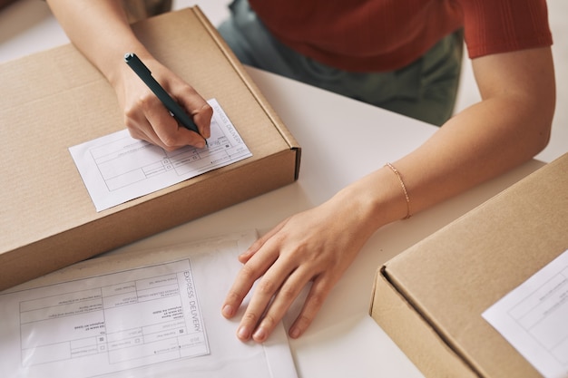 Photo close-up of woman sitting at the table signing the parcels before shipping