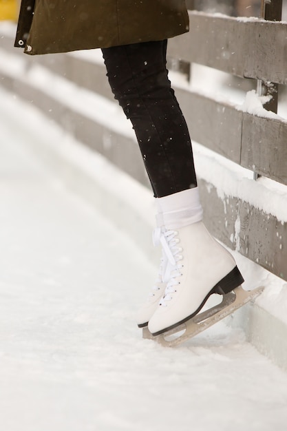 Foto chiuda su delle gambe del pattinatore della donna alla pista di pattinaggio aperta, vista laterale. pattini bianchi femminili su ghiaccio, treni vicino al muro, imparando a bilanciare. attività del fine settimana all'aperto quando fa freddo.