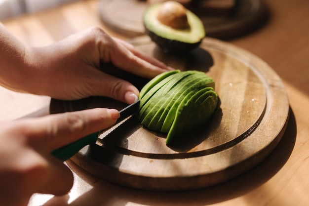 Close up of woman slicing avocado on wooden board at home Vegetarian food concept