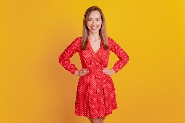 Close-up of a woman smiling hands hips wear red short dress on yellow wall