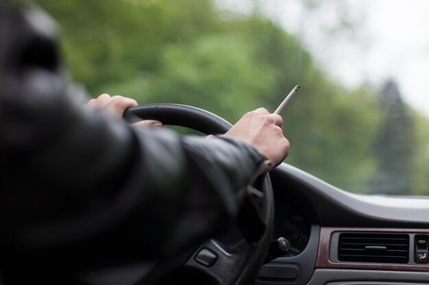 Foto close-up di una donna che fuma una sigaretta mentre guida un'auto contro un albero