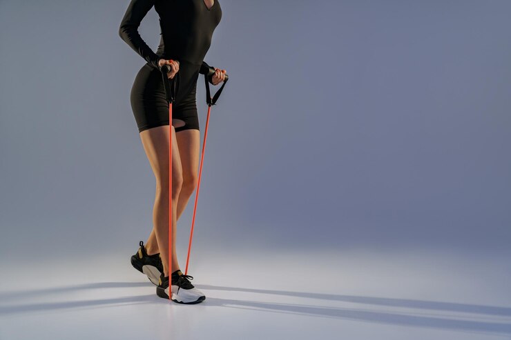 Close up of woman in sportswear performs fitness exercises with resistance band on studio background