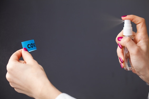 Close up of woman spraying antiseptic on coronavirus inscription.