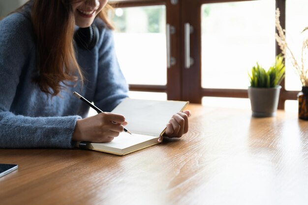 Close up of woman study online distant on laptop make note\
write in notebook sitting on desk at home smart female writer or\
student handwrite in stationery notepad planning or making\
list