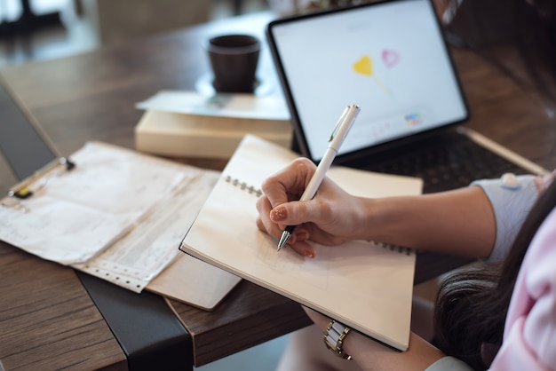 Close up of Woman taking notes on desk at cafe