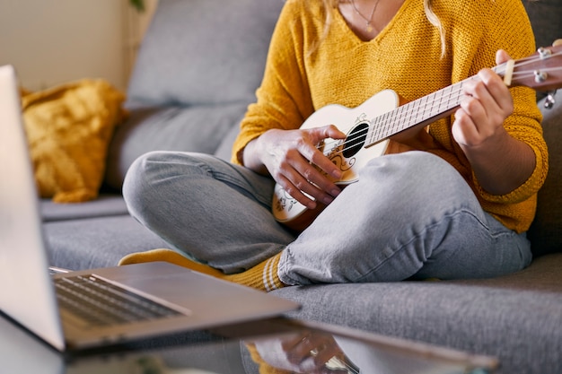 Photo close up of woman taking ukulele lessons online from her laptop during covid quarantine.