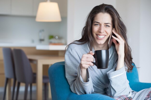 自宅のソファにカップを握りながら電話で話している女性のクローズアップ
