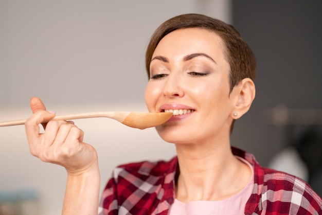 Close-up of a woman trying a cooked dish using a long wooden spoon.