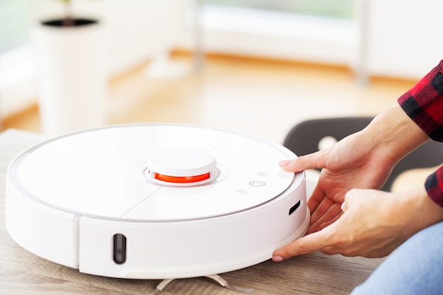 Close up of woman turns on smart robot vacuum cleaner.