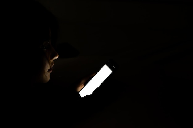 Photo close-up of woman using mobile phone in darkroom