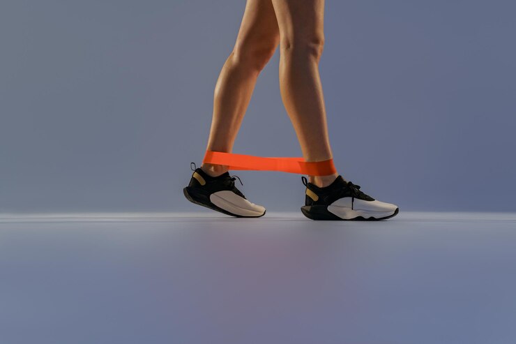 Close up of woman wearing sportswear trains legs with fitness elastic band on studio background