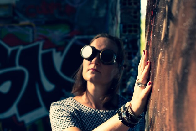Foto close-up di una donna che indossa occhiali da sole vicino al muro