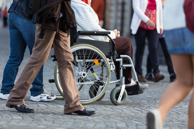 Close up of woman on a wheelchair with a helper during walk in the busy street