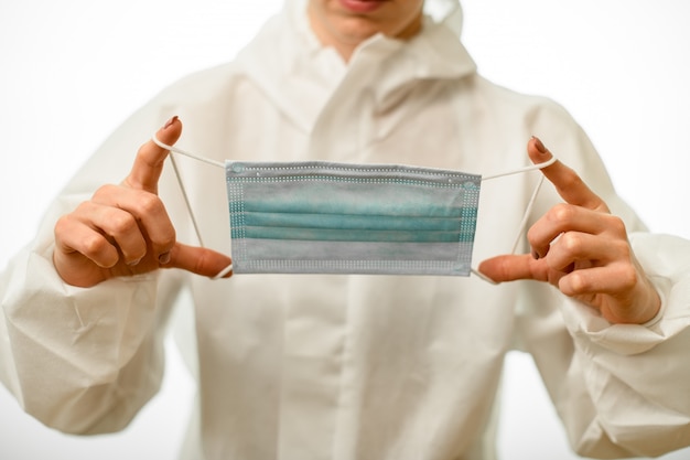 Close-up woman in white protective suit neatly holds medical mask