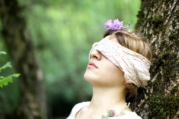 Foto close-up di una donna con una fascia cieca appoggiata al tronco di un albero