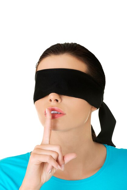 Photo close-up of woman with blindfold gesturing finger on lips against white background