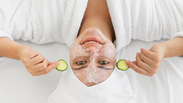 Foto donna del primo piano con crema per il viso e cetrioli