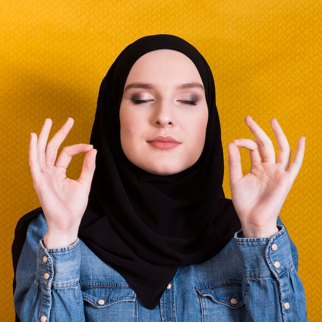 Primo piano di una donna con headcover che gesturing segno giusto e che medita su fondo