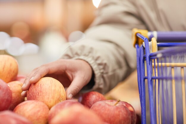 Close-up of woman with shopping cart choosing fresh apples in the market