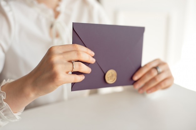 Close-up woman with slim body holding in hands the invitation card purple color square shape envelope card.