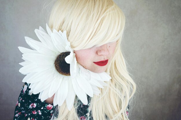 Foto close-up di una donna con un fiore bianco contro il muro