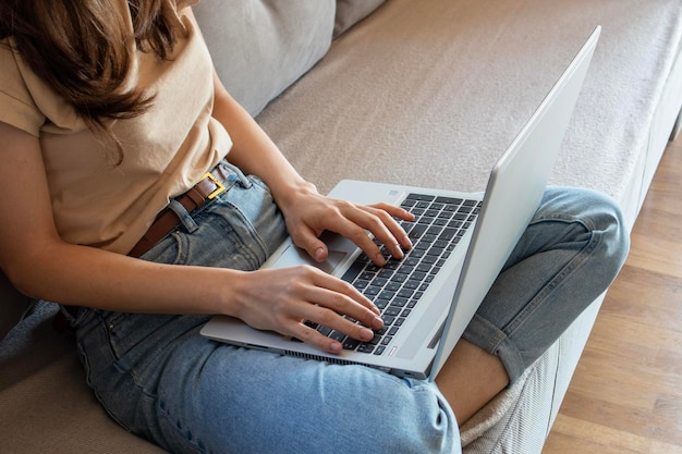 Close up of woman working from home remotely with a laptop on a sofa Comfortable workplace in cozy and stylish apartment