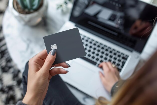 Foto close up di una donna con le mani che tiene una carta di credito grigia davanti a un computer portatile