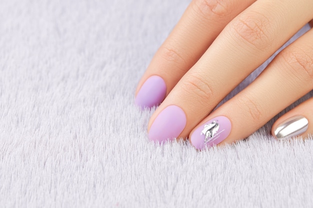 Close up womans hand with matte lavender nail design on gray furry background manicure pedicure beau...