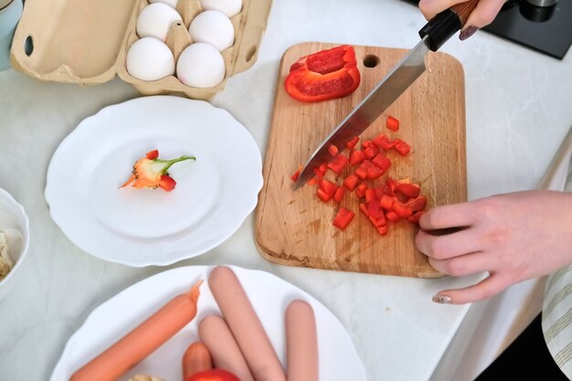 Close-up of womans hands cooking food in the kitchen, cutting paprika with knife, on cutting board