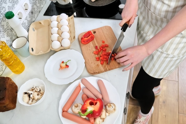 Close-up of womans hands cooking food in the kitchen, cutting paprika with knife, on cutting board