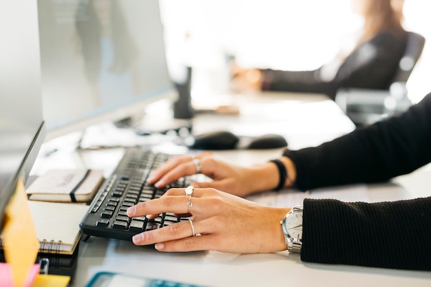 Close up of womans hands typing a computer on a messy desk