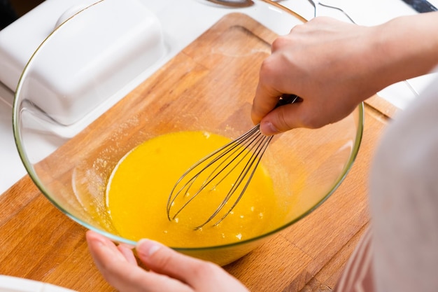 Close up of a womans hands whipping eggs for making dough on the wooden desk in the kitchen homemade...