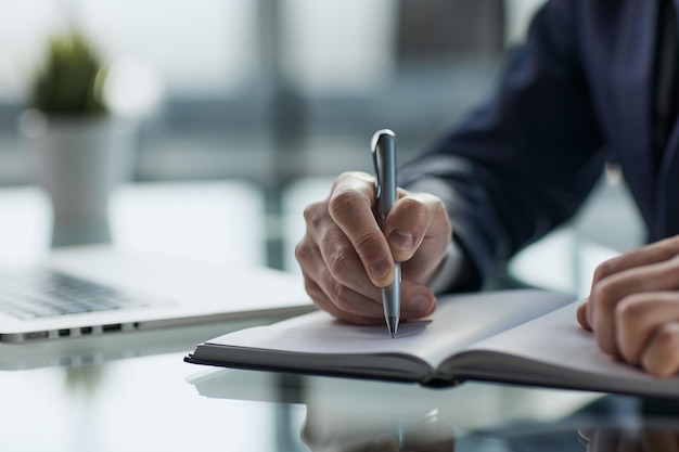 Close up of womans hands writing in spiral notepad placed on wooden desktop with various items