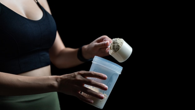 Photo close up of women with measuring scoop of whey protein and shaker bottle preparing protein shake