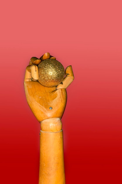 赤の背景に金色のボールを保持している木製の人間の手のクローズ アップ.