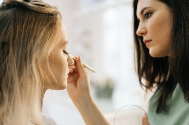 Close-up of work professional makeup artist applying eyeshadow to young pretty woman in dressing room. Concept of backstage work.