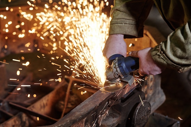 Close-up of worker using grinder for grinding metal in the plant