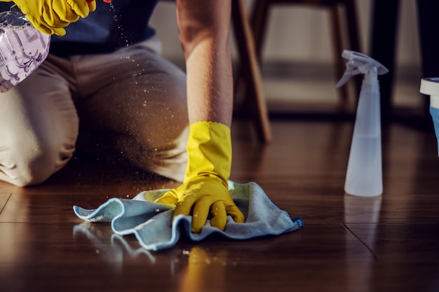 Foto close up degno uomo inginocchiato, spruzzare detergente e pulire il parquet a casa.