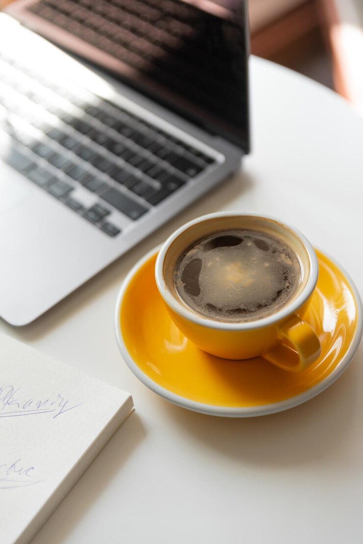 Close up of yellow cup of coffee on workspace on table near laptop Flat lay of work place of freela