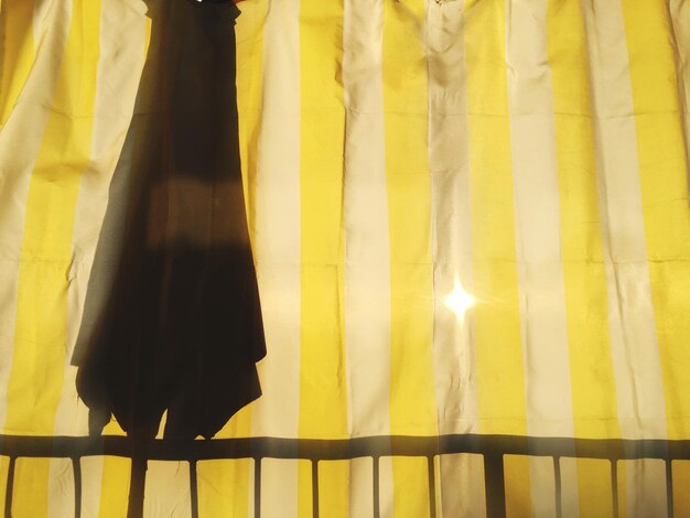 Foto close-up di una tenda gialla con la luce solare che attraversa e la silhouette di un ombrello chiuso
