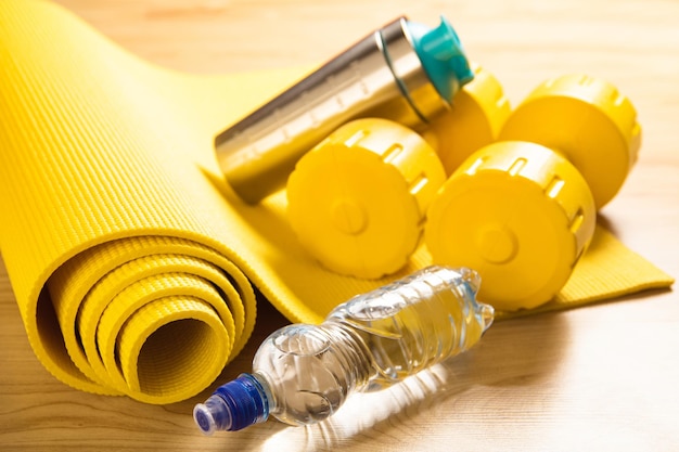 Close-up of yellow dumbbells, fitness mat and bottle of still\
water on the floor