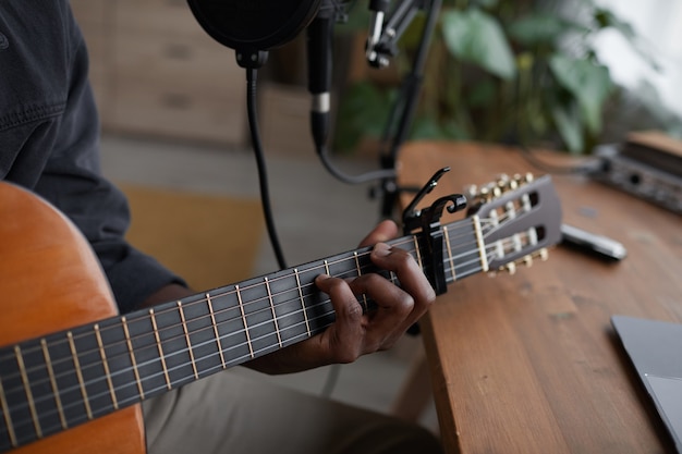 Close up of young African-American man playing guitar in home recording studio, copy space