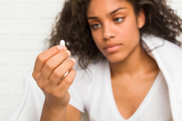 Close up of a young african american sick woman sitting on the bed taking a pill