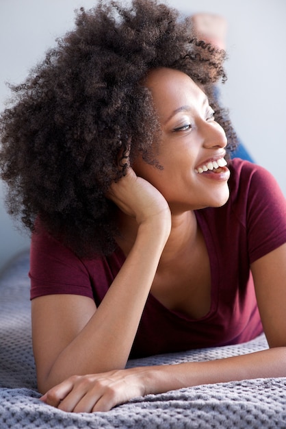 Chiuda sulla giovane donna africana che si trova sul pavimento a casa e sul sorridere