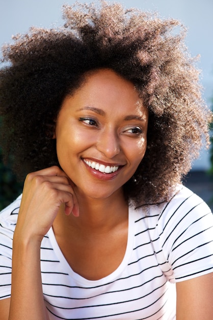 Close up young african woman with curly hair looking away and smiling outdoors