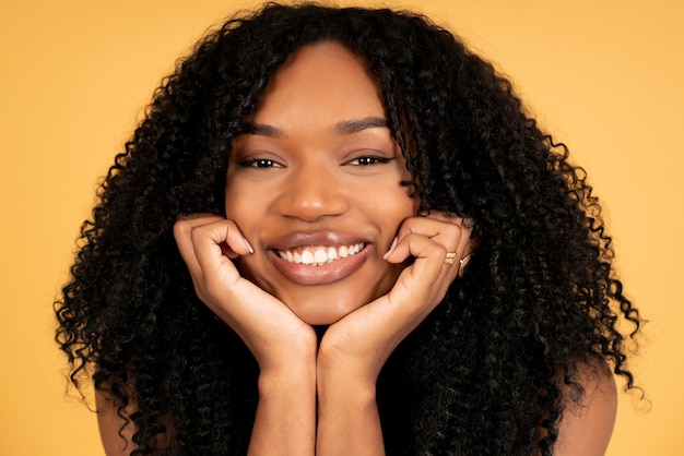 Photo close-up of a young afro woman looking at the camera and smiling while standing against isolated background.