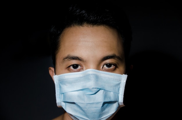 Photo close up of young asian man wearing hygienic mask with dark blackground